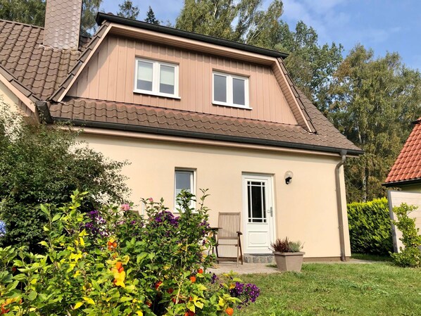 Une maison à deux étages, avec un toit recouvert de tuiles, une porte d’entrée et un petit porche agrémenté d’une chaise.