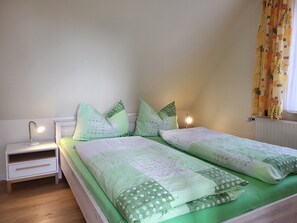 Une chambre avec deux lits, une table de chevet avec une lampe et une fenêtre avec des rideaux.