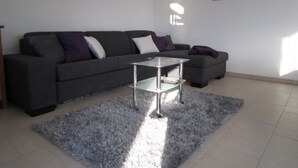 A modern living room with a grey sofa, a glass coffee table, and a grey rug.