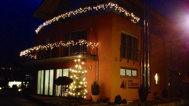 A building with a Christmas tree and lights, a sign reading 'Haus Lorenz,' and a brick pathway.