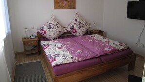 Ein Schlafzimmer mit einem Bett, zwei Nachttischen, einem an der Wand befestigten Fernseher und einem Gemälde.