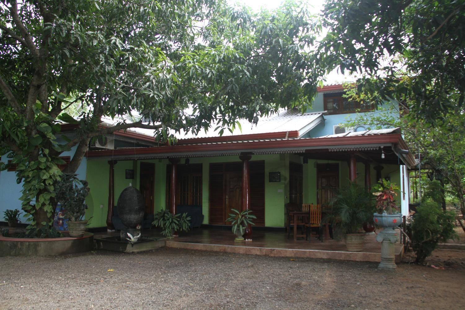 A traditional house with a porch, surrounded by lush greenery.