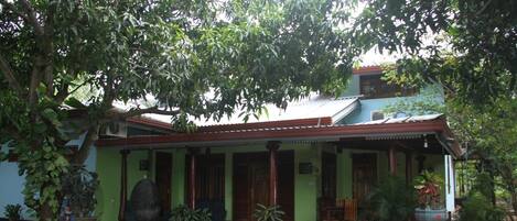 A traditional house with a porch, surrounded by lush greenery.