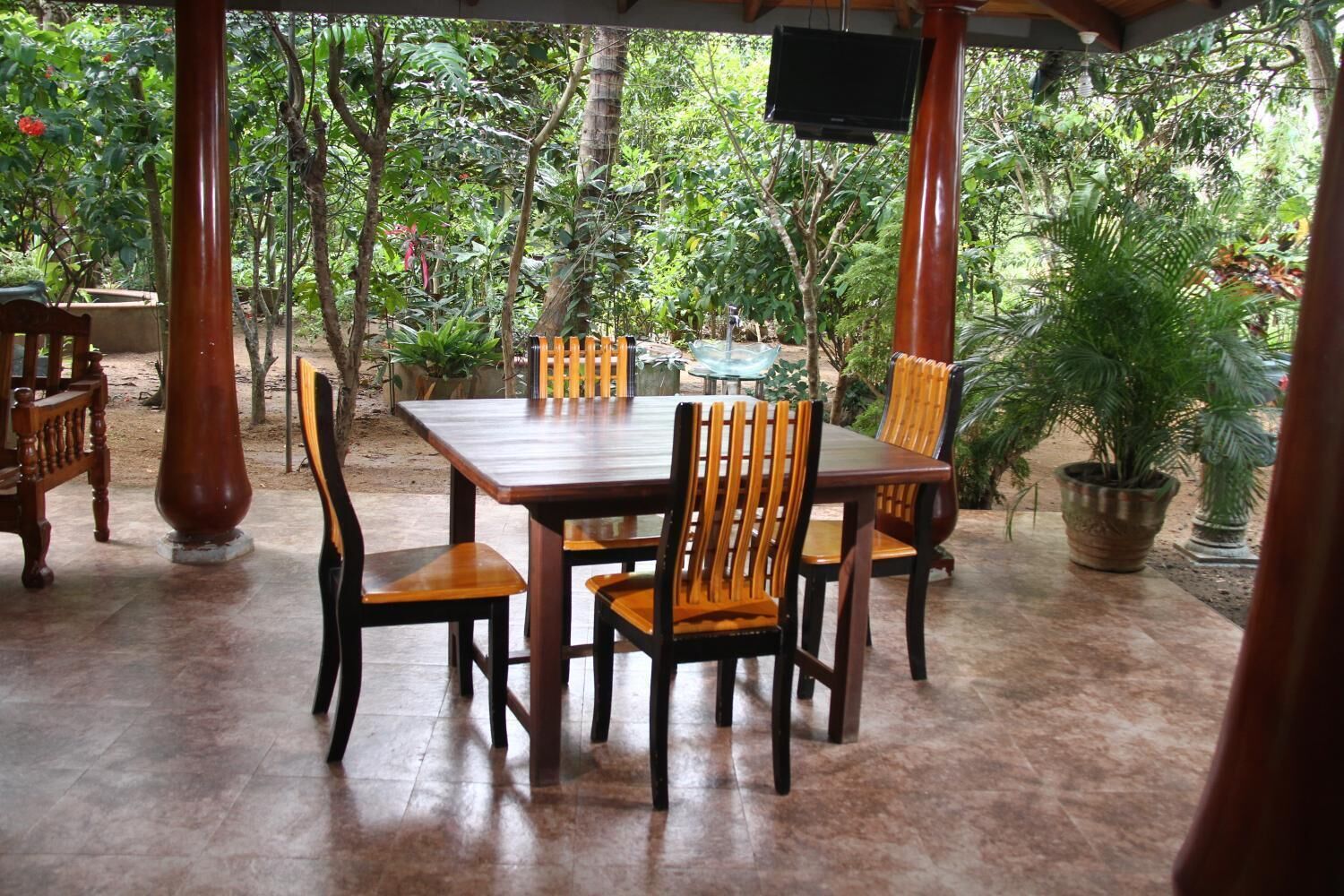 Eine Terrasse im Freien mit Holztisch und -stühlen, umgeben von Kübelpflanzen und Bäumen.