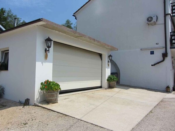 Una casa de un piso con puerta de garaje, dos macetas y un cobertizo pequeño.