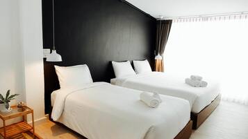 Et hotelværelse med to senge, hvide sengetøj, et lille trænatbord med en plante og en sort væg.