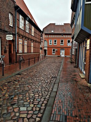 A cobblestone street lined with historic buildings, including a red brick building with a sign that reads "Fischersstr. 2".