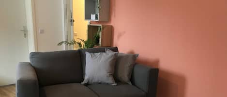 Un salon moderne avec un canapé gris, deux petites tables rondes blanches et un mur d’accent rouge.