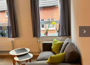 A living room with a grey sofa, a small round table, and a window with curtains.