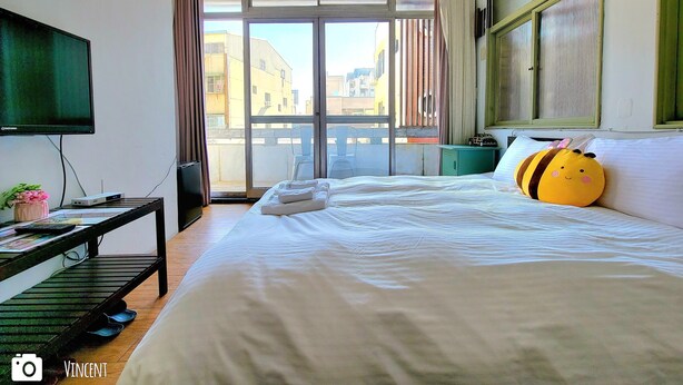 A hotel room with a bed, a TV, a desk, and a window with a view of buildings.