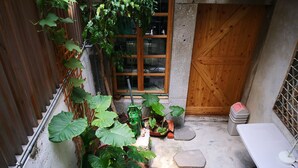 A small courtyard with a wooden door, a window, and a table with a lamp.