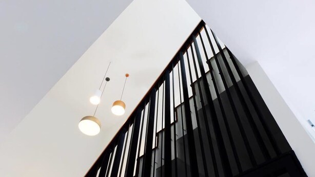 Un edificio moderno con fachada blanca y elementos verticales negros, que incluye tres lámparas colgantes.