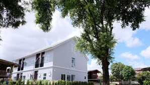 Un edificio residencial de dos pisos con fachada blanca, múltiples ventanas y un jardín cuidado con setos y árboles.