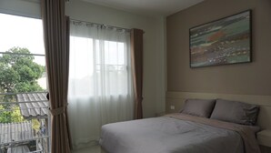 Un dormitorio con cama, cortinas, un cuadro y vistas al exterior.