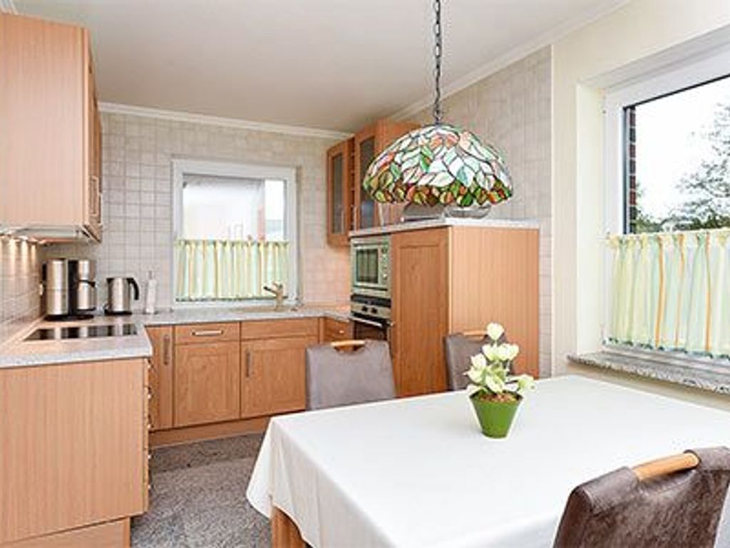A kitchen with wooden cabinets, a dining table with a white tablecloth, and a stained glass light fixture.