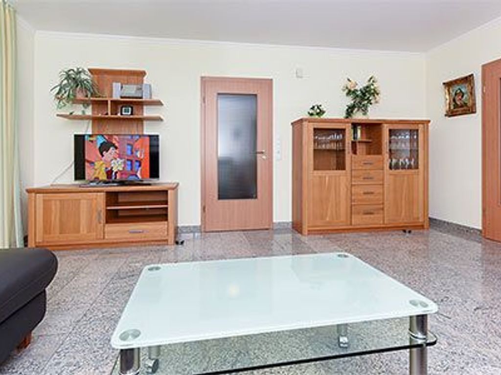 Ein Wohnzimmer mit Flachbildfernseher, Holzausstattung, einem Glastisch und einer Tür.