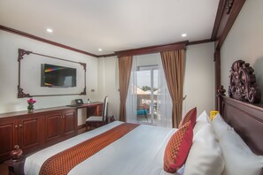 Une chambre d’hôtel avec un grand lit, un bureau avec un ordinateur portable, un téléviseur fixé au mur et une vue sur l’extérieur grâce à une porte-fenêtre coulissante.
