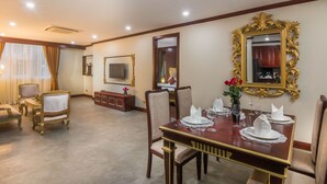 A dining area with a wooden table set for four, surrounded by upholstered chairs. A large ornate mirror and a flat-screen TV are mounted on the wall. - Anachak Angkor Suite (Siem Reap)