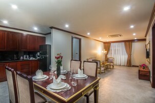 Comedor con mesa de madera dispuesta para cuatro personas, rodeada de sillas, y zona de cocina con armarios y electrodomésticos de madera.