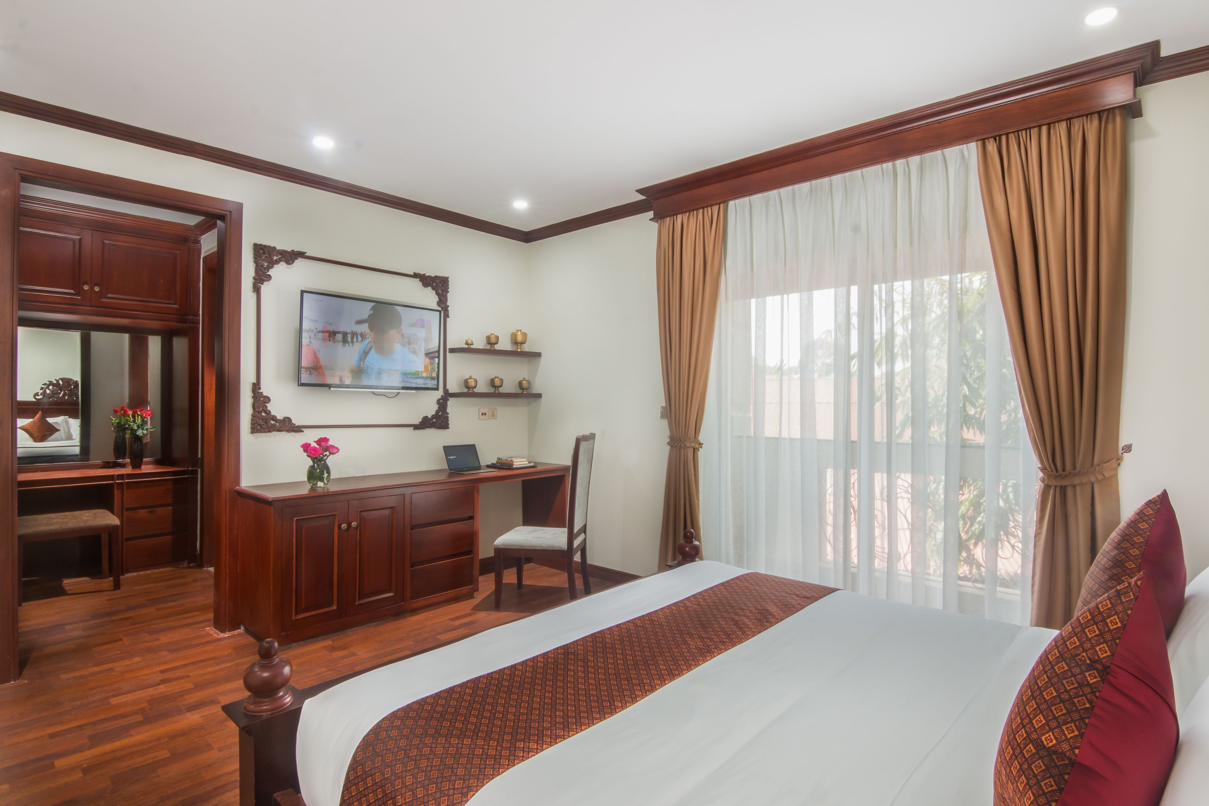 A hotel room with a large bed, a desk with a computer, a chair, a television, and a window with curtains.