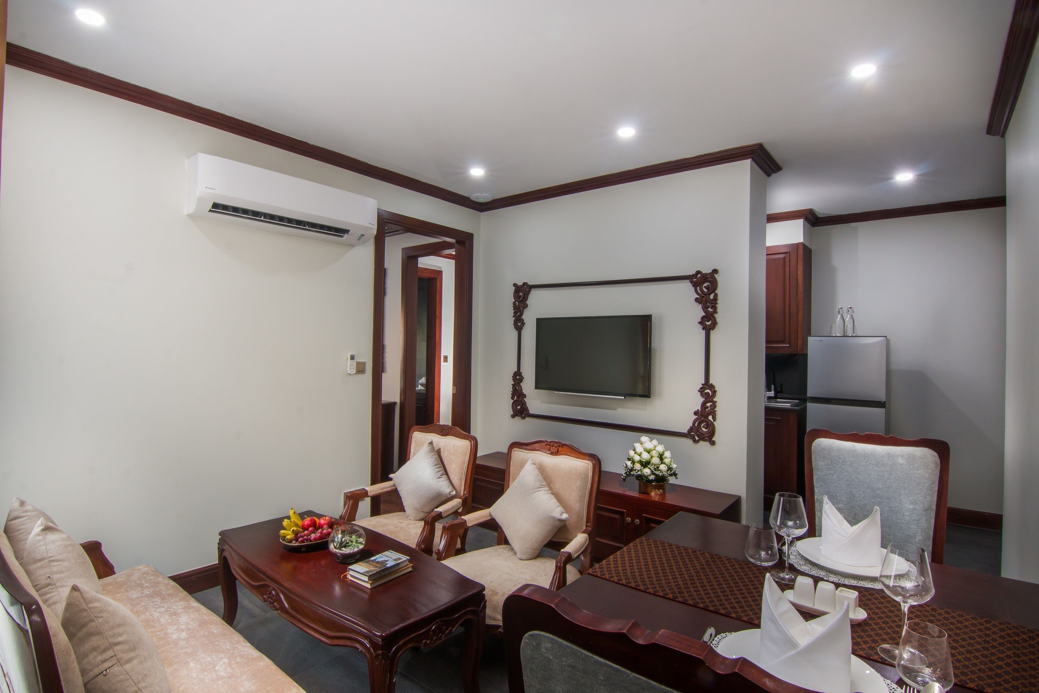 A hotel room with a dining area, a sofa, a TV mounted on the wall, and an air conditioning unit.