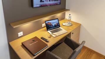 Habitación de hotel con escritorio de madera, una computadora portátil, control remoto, libreta y botella de agua.