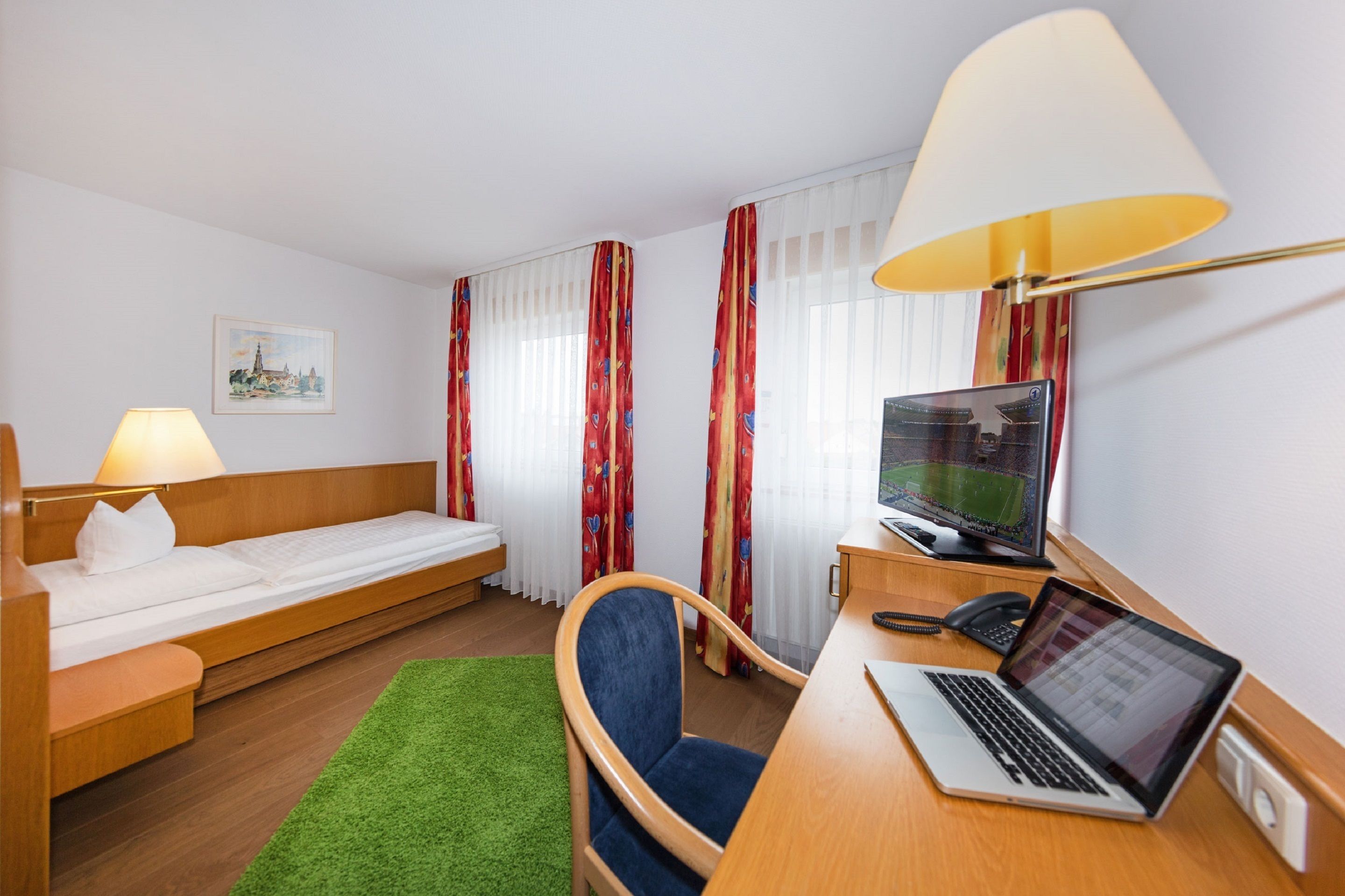 A hotel room with a bed, desk, chair, and a TV.