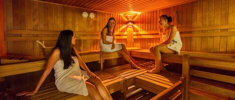 Una sauna amb grans bancs de fusta, una làmpada penjant al centre i una paret de fusta amb un rellotge.