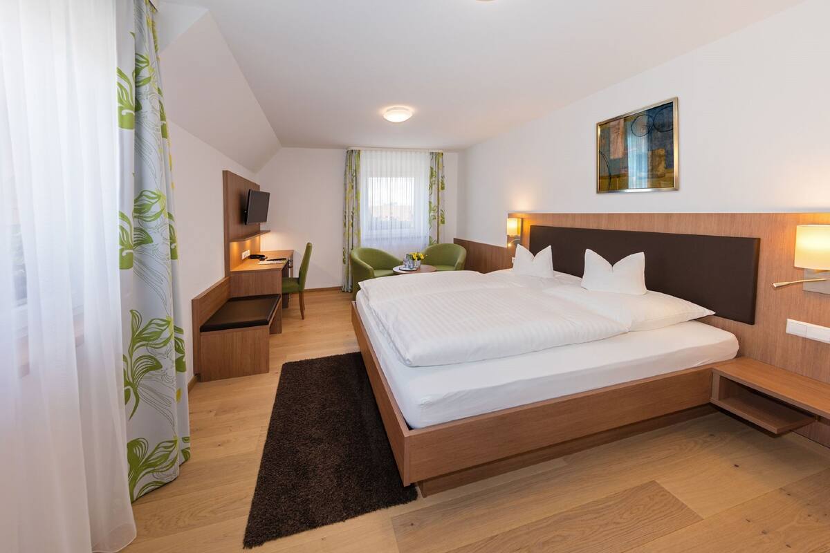 A hotel room with a large bed, a desk with a chair, a TV, and a painting on the wall.