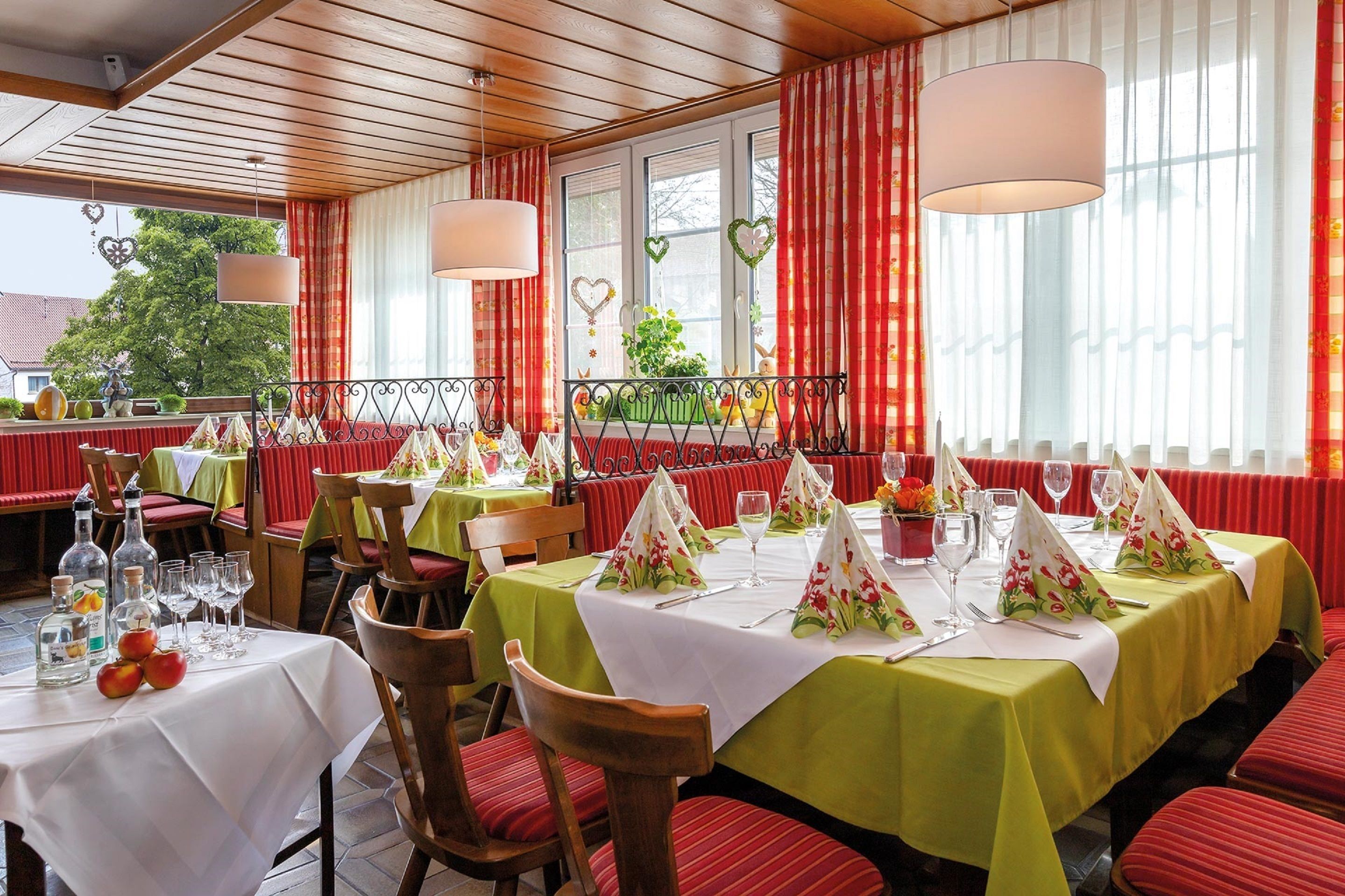 Un restaurant où les tables sont dressées pour le repas, avec des nappes rouges et vertes et des décorations en forme de cœur.