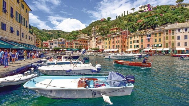 Un port de plaisance où sont amarrés des bateaux, entouré de bâtiments aux couleurs vives et bordé d’une colline.