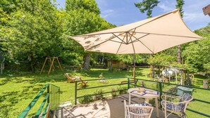 Une terrasse avec une table et des chaises, une balançoire et un grand parasol.