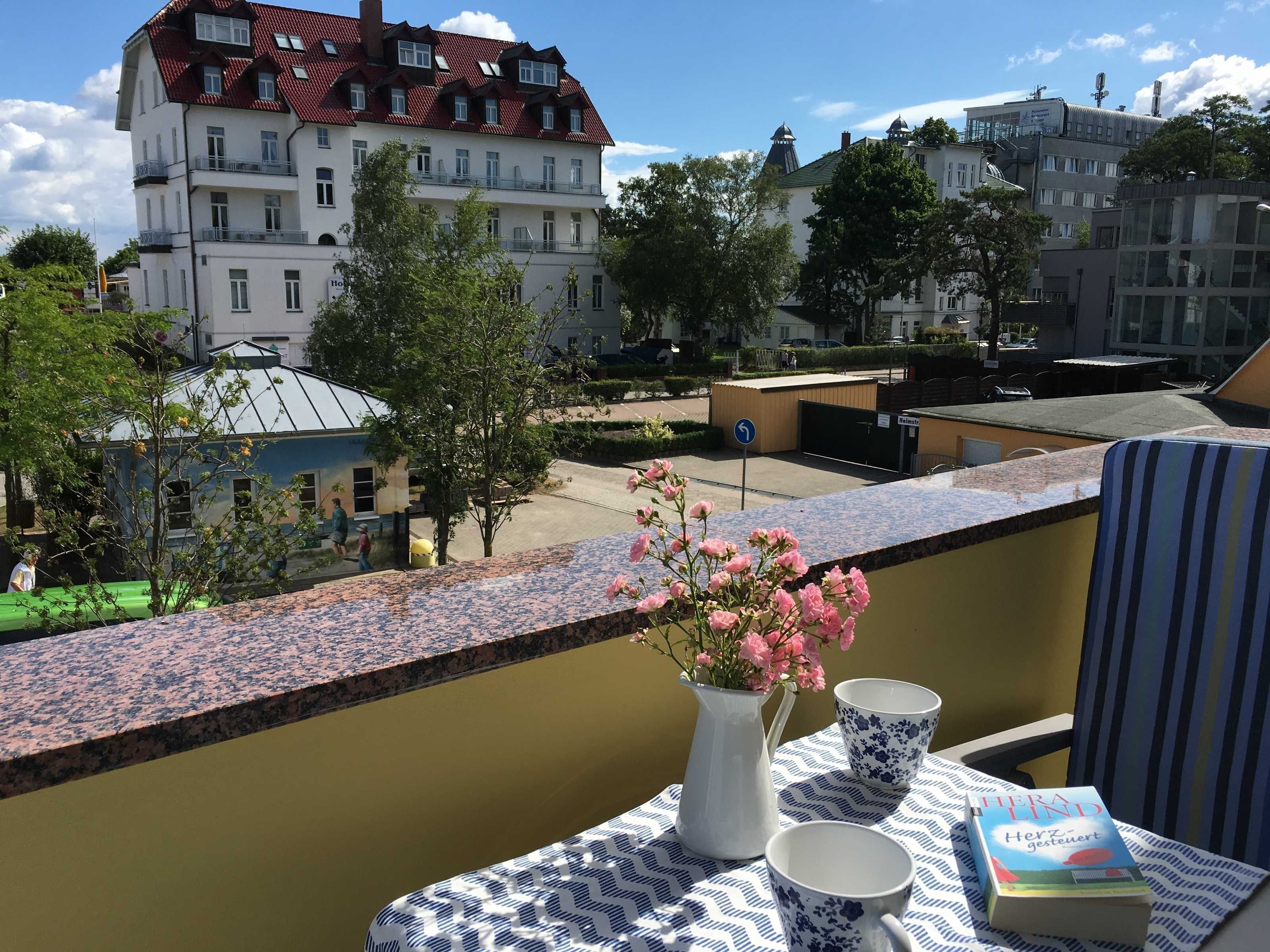 Ein Balkon mit Tisch, Blumen in einer Vase und einem Buch.
