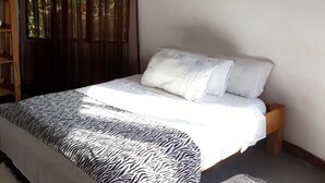 A bedroom with a bed, a window with curtains, a wall-mounted decoration, and a wooden shelf.