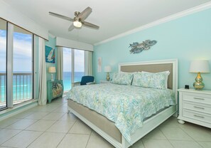Quarto com cama, ventoinha no teto, mesa de cabeceira, abajur, cômoda e vista para o mar.