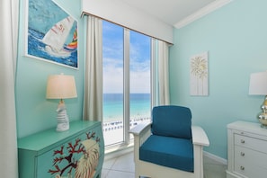 Una habitación con vista al mar, una silla, un aparador y una lámpara.