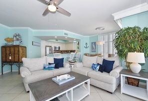 A living room with a ceiling fan, two sofas, a coffee table, and a kitchen in the background. - Spacious 10th Floor Beachfront Condo w/ Stunning Views in Central Destin! 🌅🐬 (Destin)