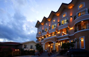 A multi-story hotel with balconies, a central entrance, and outdoor seating areas.