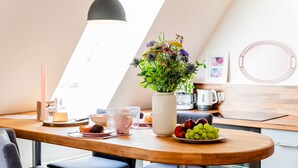 A dining area with a wooden table, a vase of flowers, a plate of fruit, and a coffee machine in the background. - Smile vacation apartment right on the beach in Wassersleben (Harrislee)