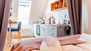 A modern bedroom with a bed, a bedside table, a window, and a view of a kitchen area. - Smile vacation apartment right on the beach in Wassersleben (Harrislee)
