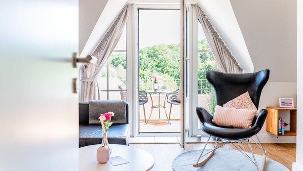 A modern room with a black leather chair, a small round table, and a sofa. There is a glass door leading to an outdoor area with a table and chairs. - Smile vacation apartment right on the beach in Wassersleben (Harrislee)