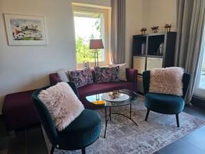 Ein Wohnzimmer mit einer Couch, zwei Sessel, einem Couchtisch, einer Lampe und einem Gemälde an der Wand.