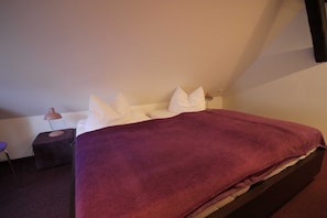 Ein Einzelbett mit einer violetten Decke, weißen Kissen und einem Nachttisch mit einer Lampe.
