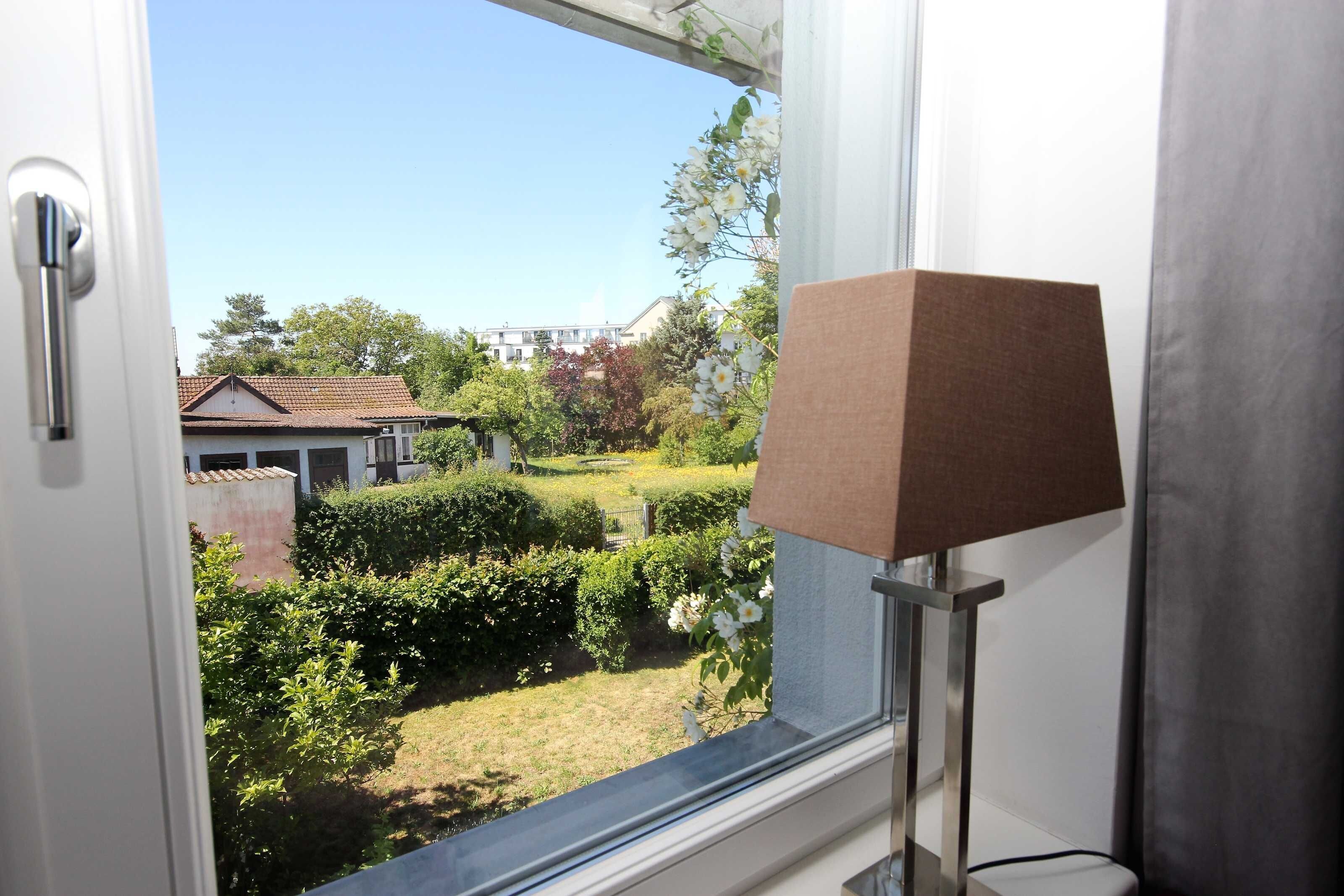 Une fenêtre donnant sur un jardin et un bâtiment situé de l’autre côté de la rue.