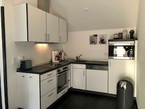 A modern kitchen with white cabinets, a coffee machine, a dishwasher, and a trash bin.