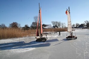 Two sailboats on a frozen lake with bare trees and houses in the background. - Vacation apartment Christl - Holiday apartment Christ`l (Wustrow)