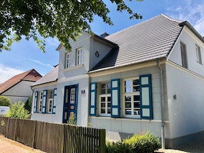 Ein zweistöckiges Gebäude mit weißer Fassade, blauen Fensterläden und einem Ziegeldach.