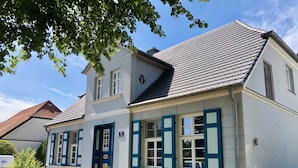 En toetages bygning med en hvid facade, blå skodder og et tag med tegltagsten.