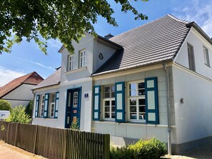 Ein zweistöckiges Gebäude mit weißer Fassade, blauen Fensterläden und einem Ziegeldach.