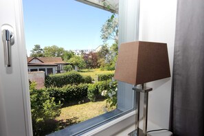 Ein Fenster mit Blick auf einen Garten und ein Gebäude gegenüber.